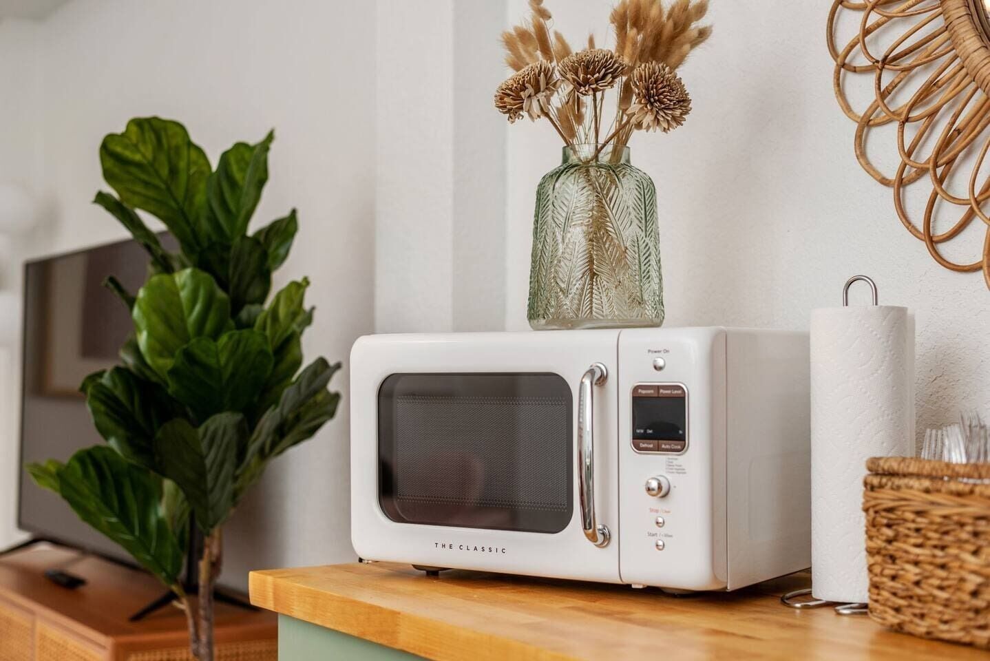 A white microwave oven on a wooden countertop with a glass vase containing dried flowers on top.