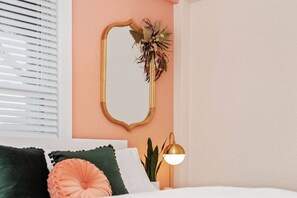 A bedroom with a bed, pillows, a bedside lamp, a mirror, and a wall-mounted plant.