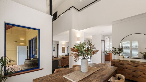 Een modern interieur met een houten eettafel, een grote spiegel, en uitzicht op een keuken en woonruimte.