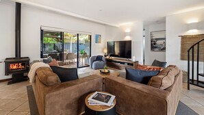Een woonkamer met een open haard, banken, een televisie en een eethoek met toegang tot buiten.
