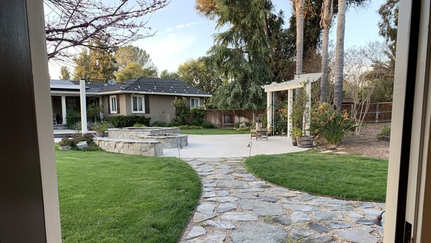 A stone pathway leading to a patio area with a pergola, surrounded by well-maintained grass and trees. - Cottage studio (Poway)