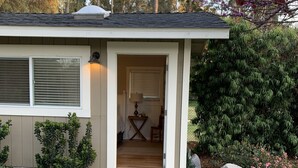 A house with a stone pathway leading to the entrance, a small porch, and a garden with various plants and a large rock. - Cottage studio (Poway)