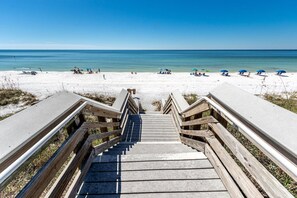A wooden staircase leading to a beach with clear blue water and white sand.