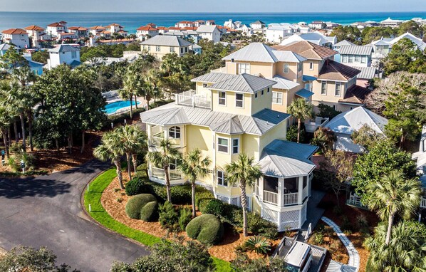 A coastal residential area with houses featuring red-tiled roofs, a central house with a large balcony, and a swimming pool.