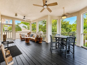 A covered outdoor deck with a sofa, chairs, a table, and ceiling fans.