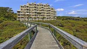 Un muelle de madera que conduce a un edificio de varios pisos con balcones, rodeado de exuberante follaje.