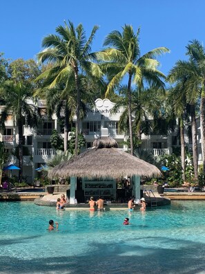 A resort pool area with palm trees and a thatched-roof structure. - **Complimentary Suite Upgrade** Romance at The Beach Club (Palm Cove)