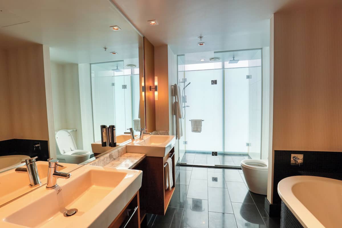 A modern bathroom with dual sinks, a large mirror, and a glass-enclosed shower area.