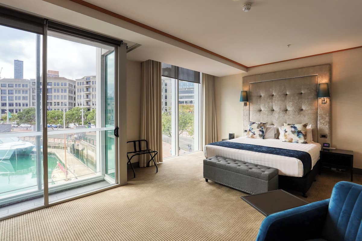 A hotel room with a large bed, a desk, a chair, a view of the city, and a balcony.