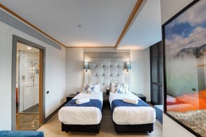 A hotel room with two beds, a large window with blinds, a headboard with a tufted design, and a framed artwork on the wall.