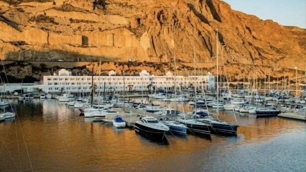 A marina with multiple boats docked, a large building with multiple windows, and a rocky cliff in the background. - Sunny Seaside Apartment in Aguadulce (AGUADULCE)