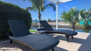 Deux fauteuils de jardin au design tressé, placés sur une terrasse en béton offrant une vue sur un plan d’eau et des palmiers.