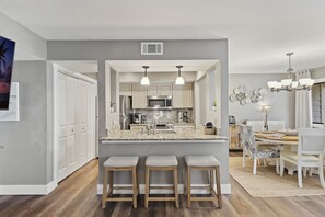 A modern kitchen with a central island, bar stools, and a dining area with a chandelier.