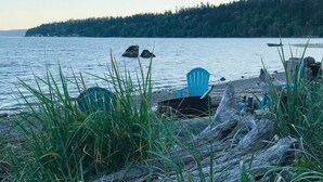 A lakeside view with a chair and logs. - Waterfront home, steps to the beach in protected bay!  Birding, kayaking, swim. (Anacortes)