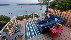 A deck with a sofa, chairs, and a table, overlooking a body of water with boats. - Waterfront home, steps to the beach in protected bay!  Birding, kayaking, swim. (Anacortes)