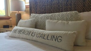 A neatly made bed with a pillow that reads "THE BEACH IS CALLING." - Waterfront home, steps to the beach in protected bay!  Birding, kayaking, swim. (Anacortes)