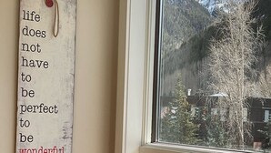 A room with a window overlooking a snowy mountain landscape, a brown leather chair, and a motivational quote on the wall.