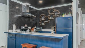 A modern kitchen with a blue island, stainless steel appliances, and a hexagonal backsplash.