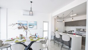 A modern kitchen with a central island, bar stools, and a dining area with a table set for four. - Villa Prol26, Stunning 3bdr Protaras Villa with Pool, Close to Fig Tree Bay (Protaras)