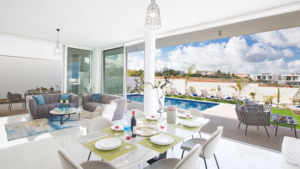 A modern dining area with a pool view, a sofa set, and a dining table set for six. - Villa Prol26, Stunning 3bdr Protaras Villa with Pool, Close to Fig Tree Bay (Protaras)