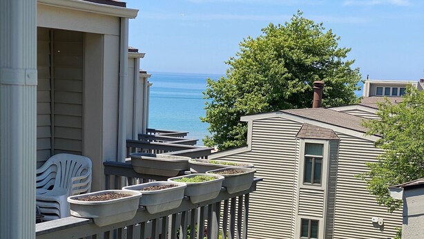 A residential area with a wooden deck, potted plants, and a view of the ocean. - South Haven Condo w/ LAKE MICHIGAN + LIGHTHOUSE VIEWS w/ POOL + PRIVATE BEACH  (South Haven)