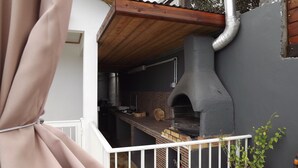 A brick oven under a wooden roof, a white railing, and a plant.