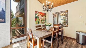 A dining area with a wooden table, chairs, a chandelier, a painting, and a view of a balcony.