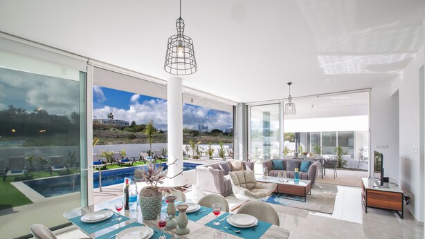 A modern dining area with a table set for four, large windows, and a view of a swimming pool and landscape. - Villa Prol21,fantastic 3bdr Protaras Villa with Pool,close to Fig Tree Bay Beach (Protaras)