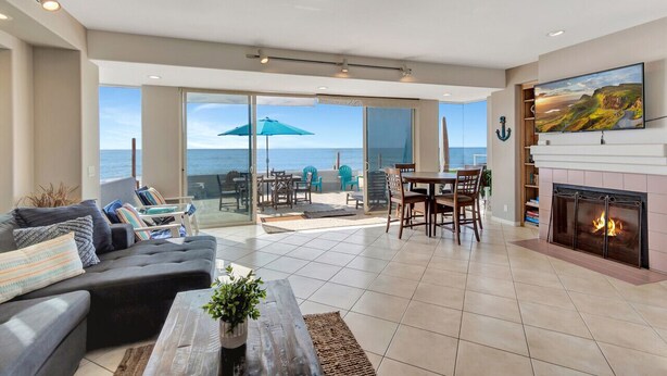A spacious living room with a large window overlooking the sea, a fireplace, and a dining area with outdoor seating. - Beach access escape w/ oceanfront deck- STR16-0534 (Dana Point)