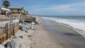 A beach with rocky shoreline, a wooden fence, and buildings in the background. - Beach access escape w/ oceanfront deck- STR16-0534 (Dana Point)