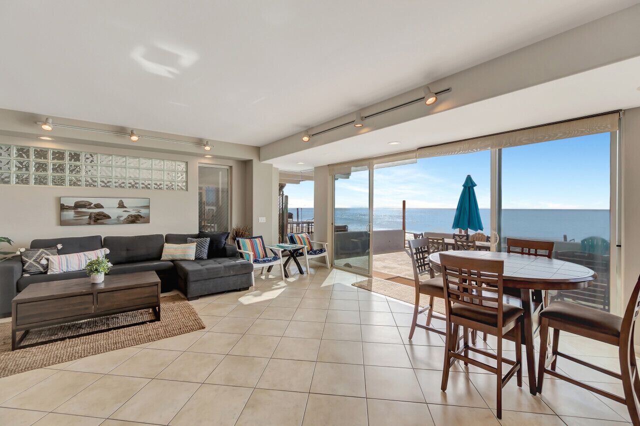 A spacious living area with a large window overlooking the sea, a dining area with a table and chairs, and a cozy seating area with a sofa and coffee table.