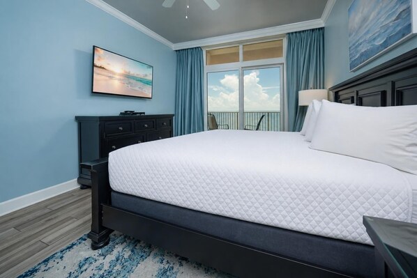 A bedroom with a large bed, a dresser, a nightstand, a painting, and a view of the sky through the window.