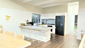 Una cocina moderna con armarios blancos, una isla central con taburetes de bar, un refrigerador negro y un comedor con mesa y sillas de madera.