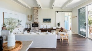 Una sala de estar moderna con chimenea, sofás blancos, una mesa de centro y un ventanal grande.