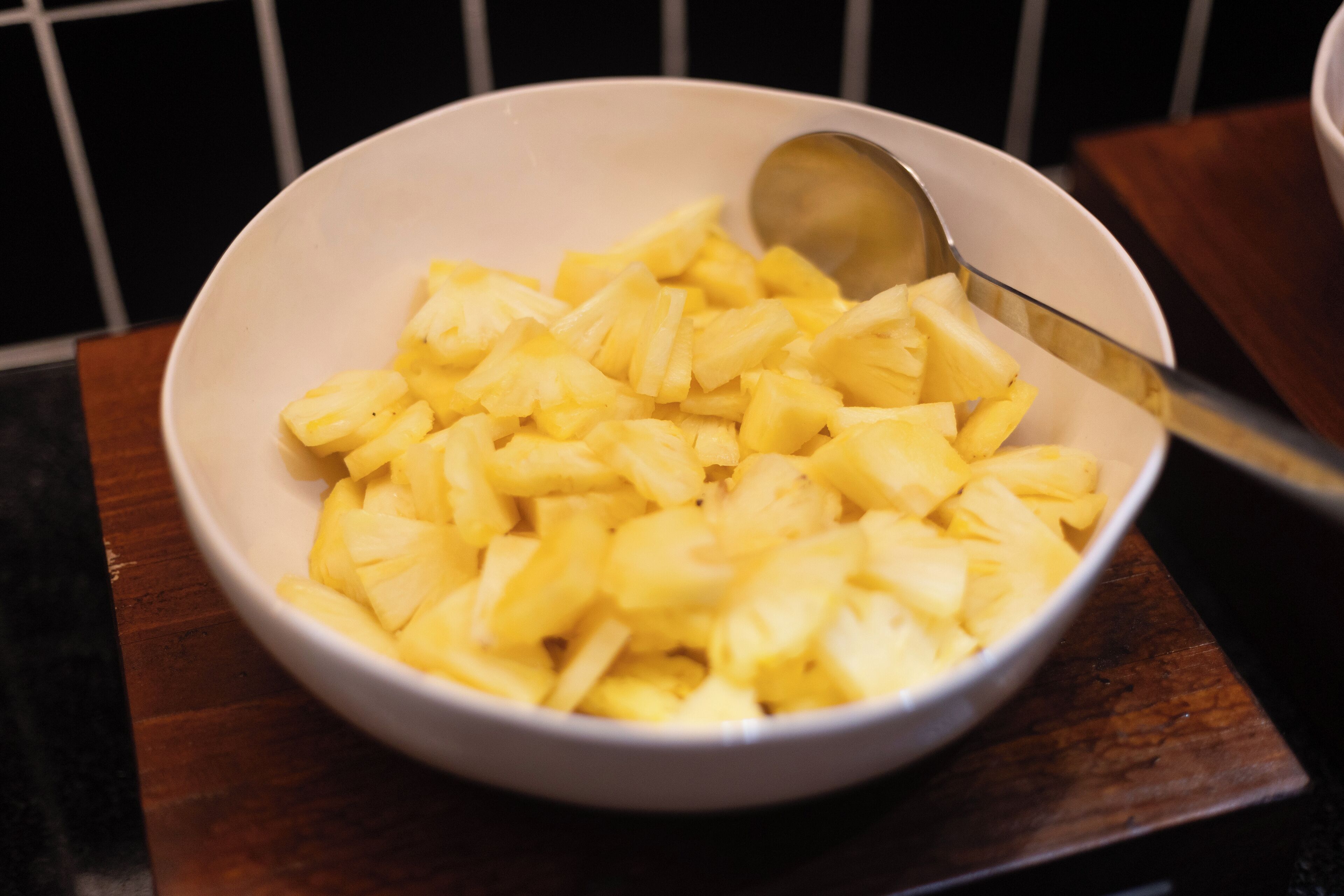 A bowl of chopped pineapple on a wooden surface.