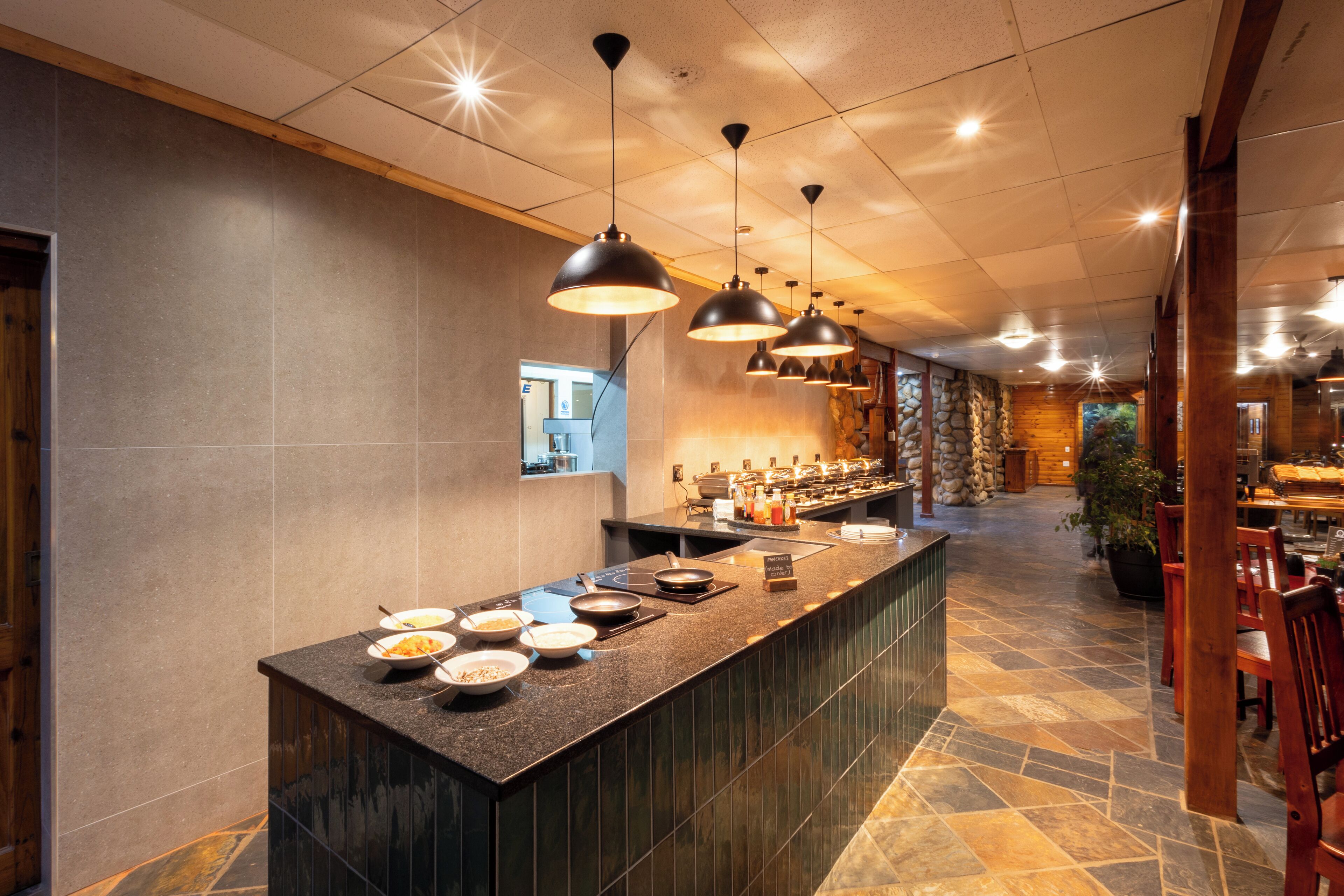Un moderno vestíbulo de hotel con una zona de bar central que ofrece una variedad de comidas y un fondo de pared de piedra.