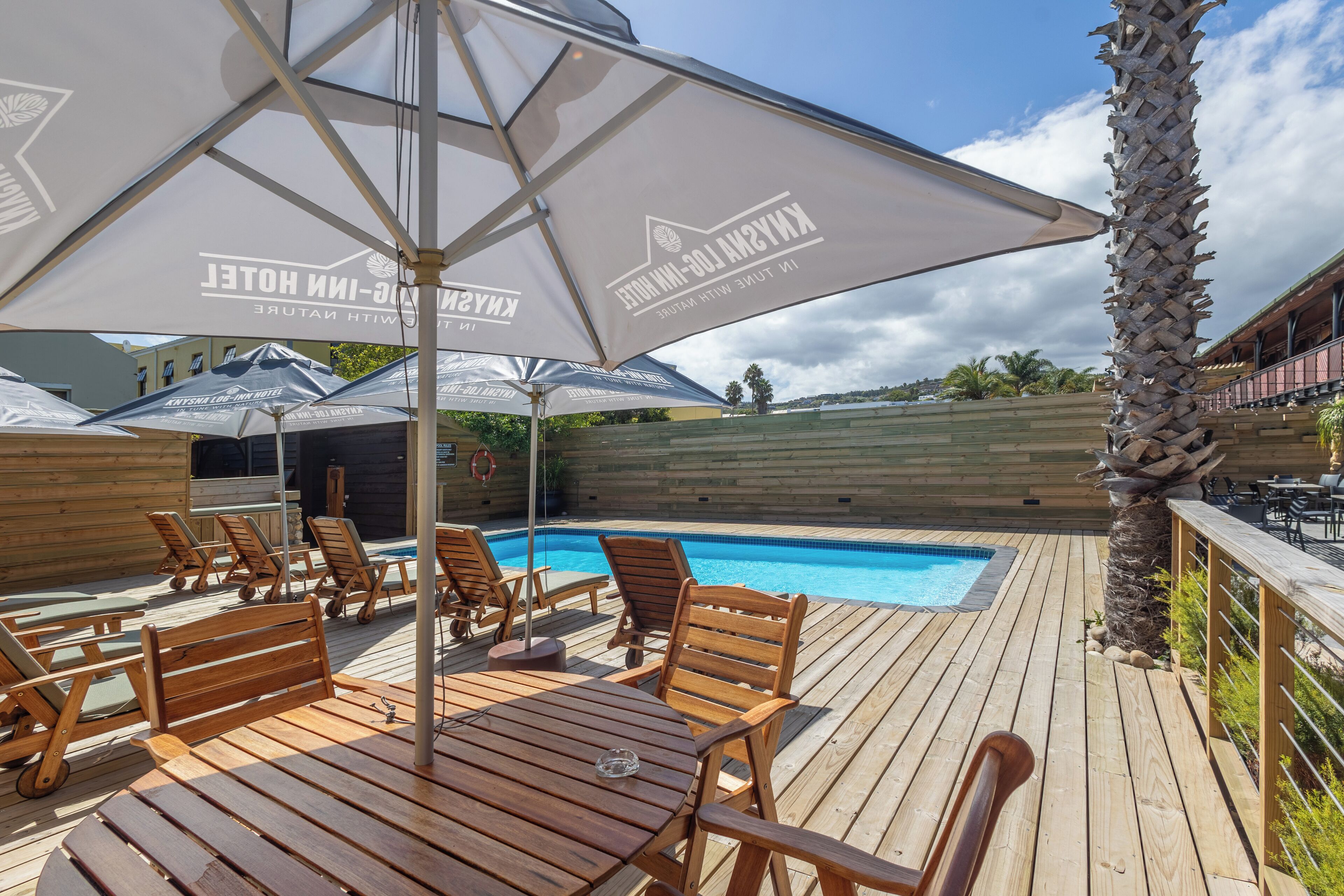 A wooden deck with lounge chairs and umbrellas, a pool, and a wooden fence.