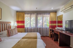 Habitación de hotel con dos camas, un escritorio, un televisor y una ventana con cortinas.