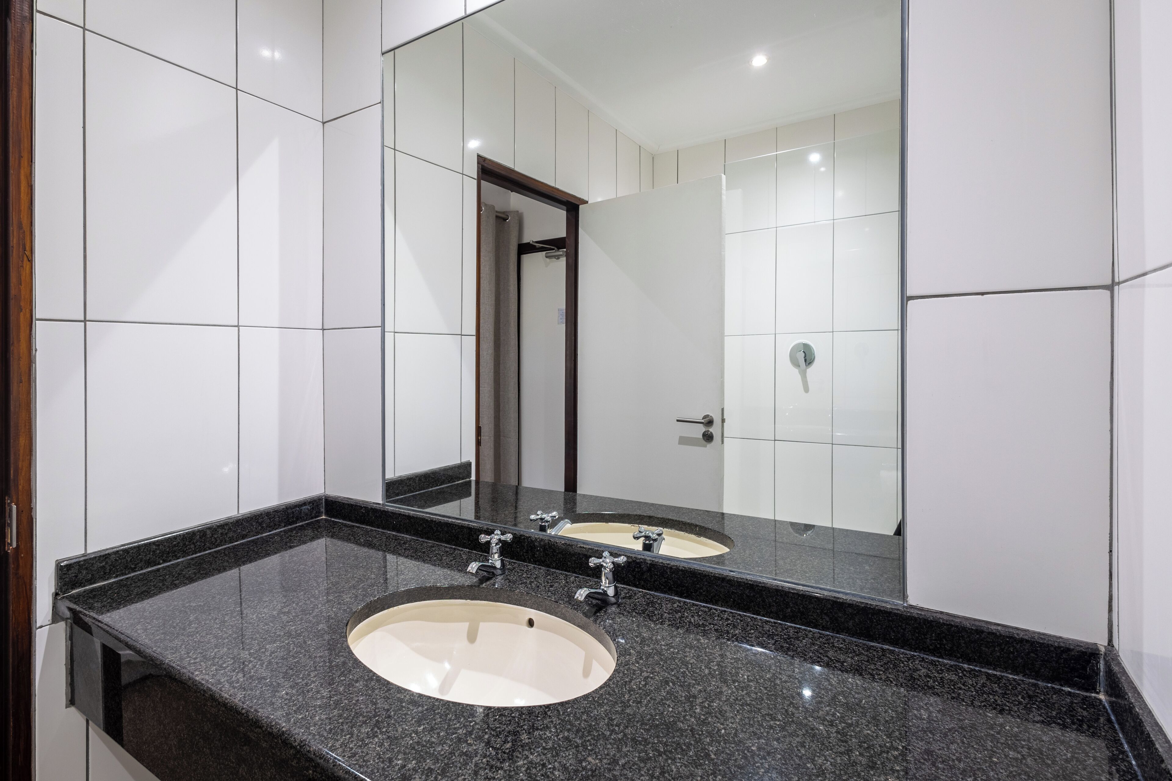 A bathroom with two sinks, a large mirror, and white tiled walls.