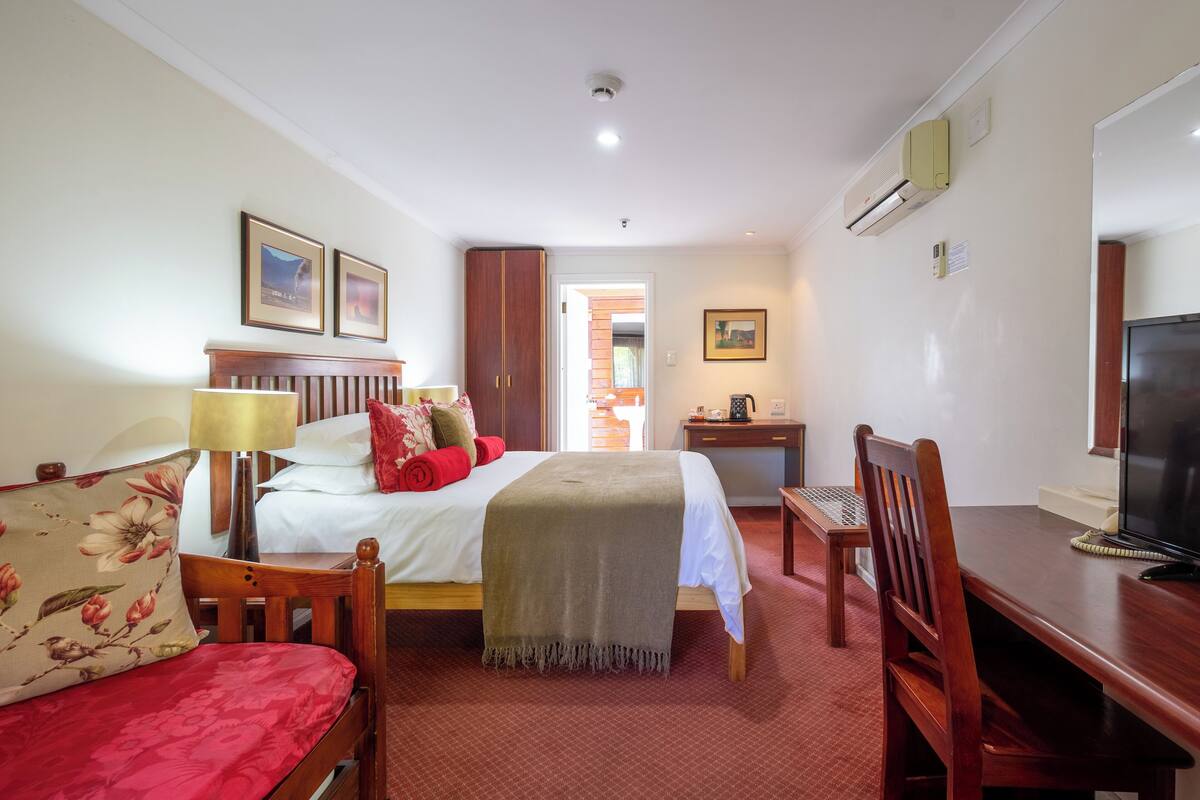 Habitación de hotel con cama, escritorio, silla, televisión y puerta que da a otra habitación.