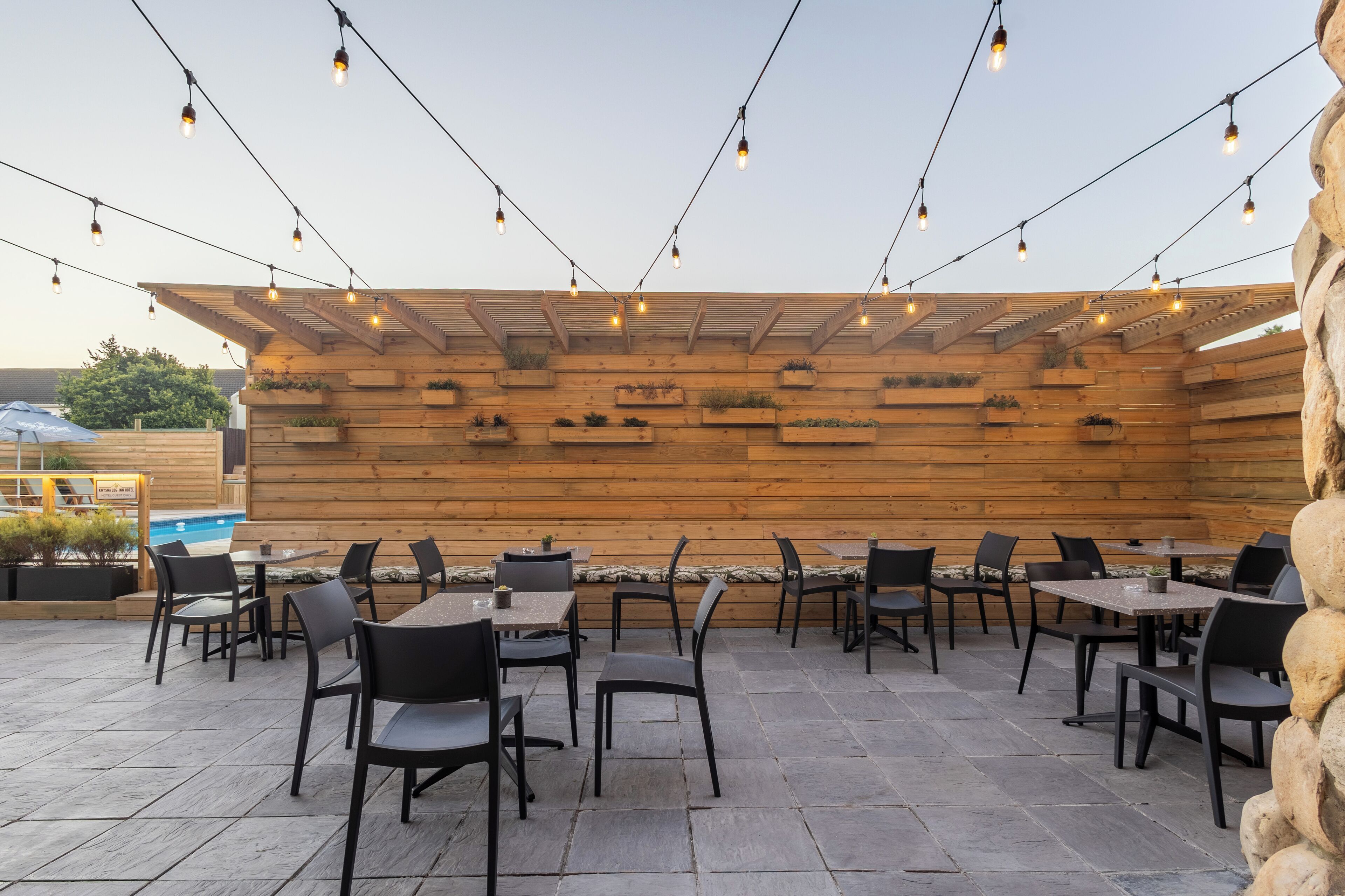 An outdoor patio with stone flooring, wooden walls, and black chairs and tables.