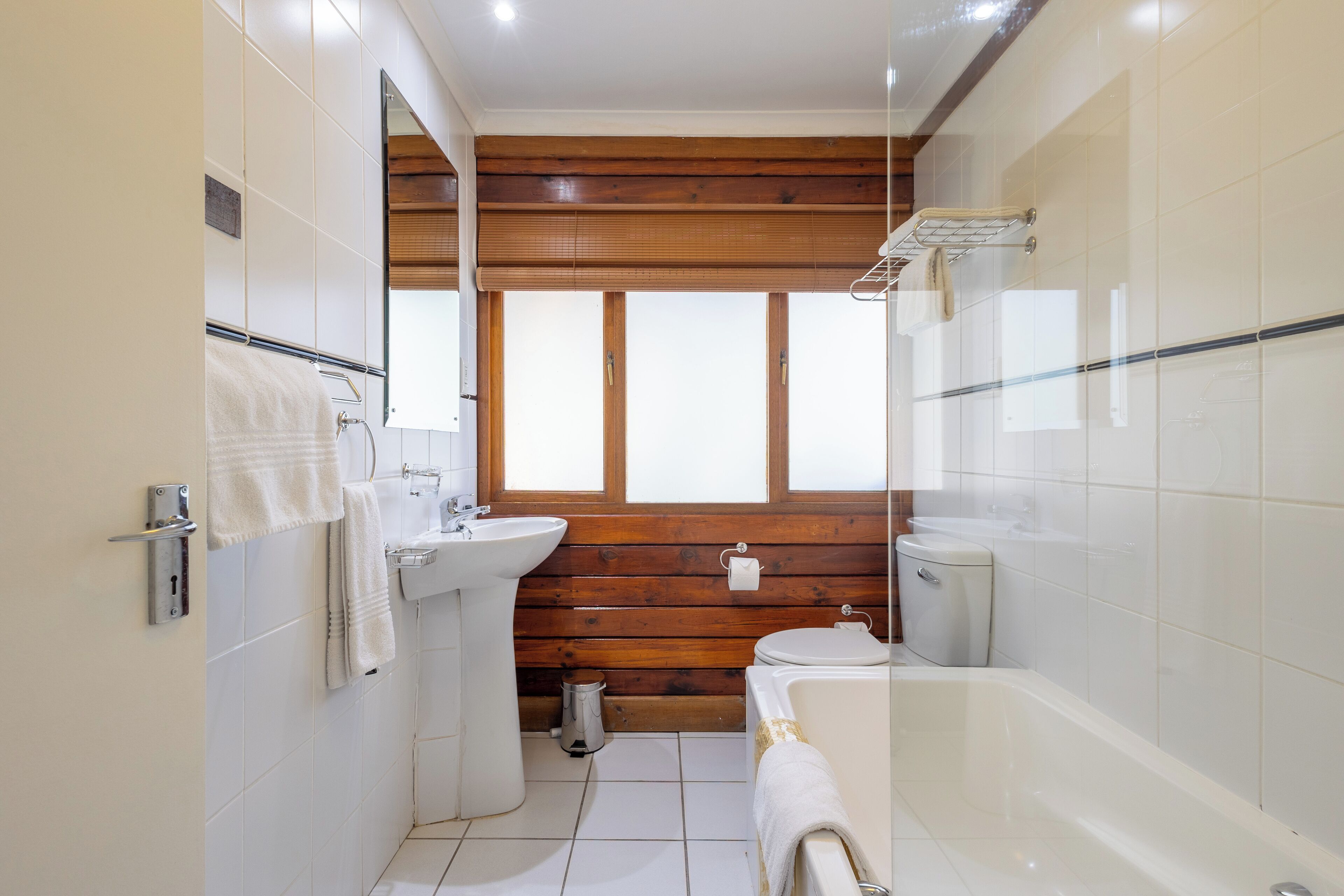 A bathroom with a wooden wall, a sink, toilet, and a bathtub.