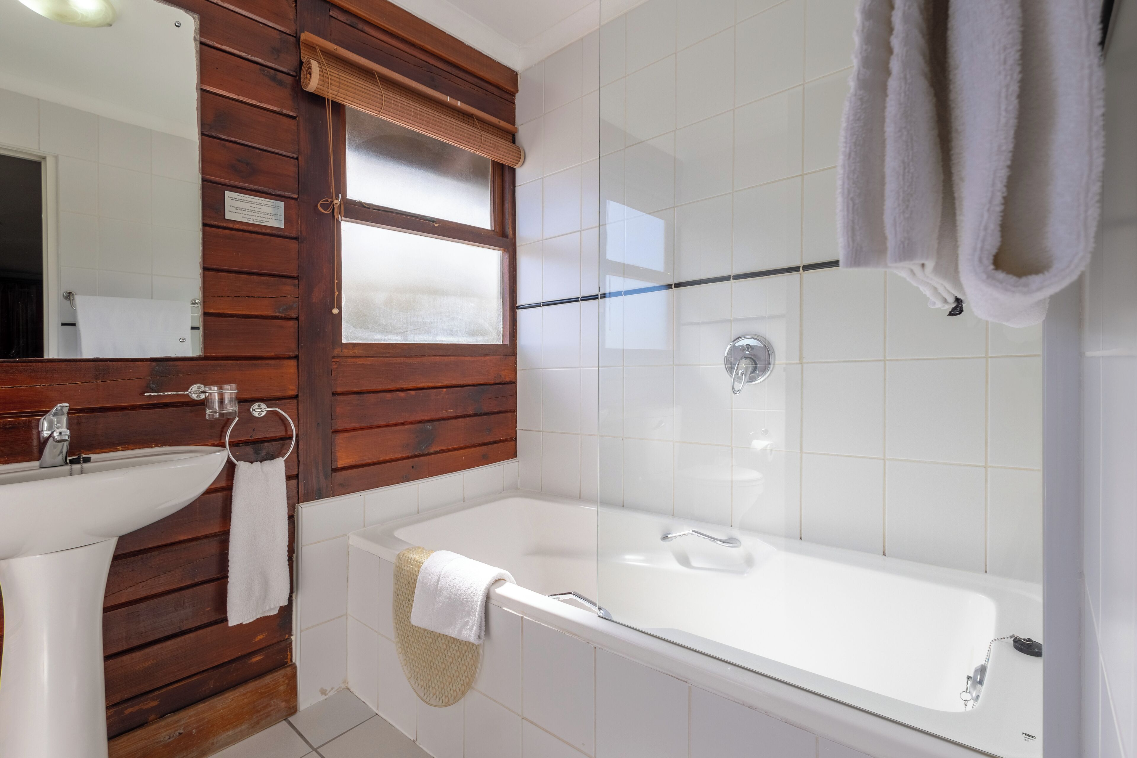 A bathroom with a wooden vanity, a white sink, a bathtub, and a glass shower enclosure.