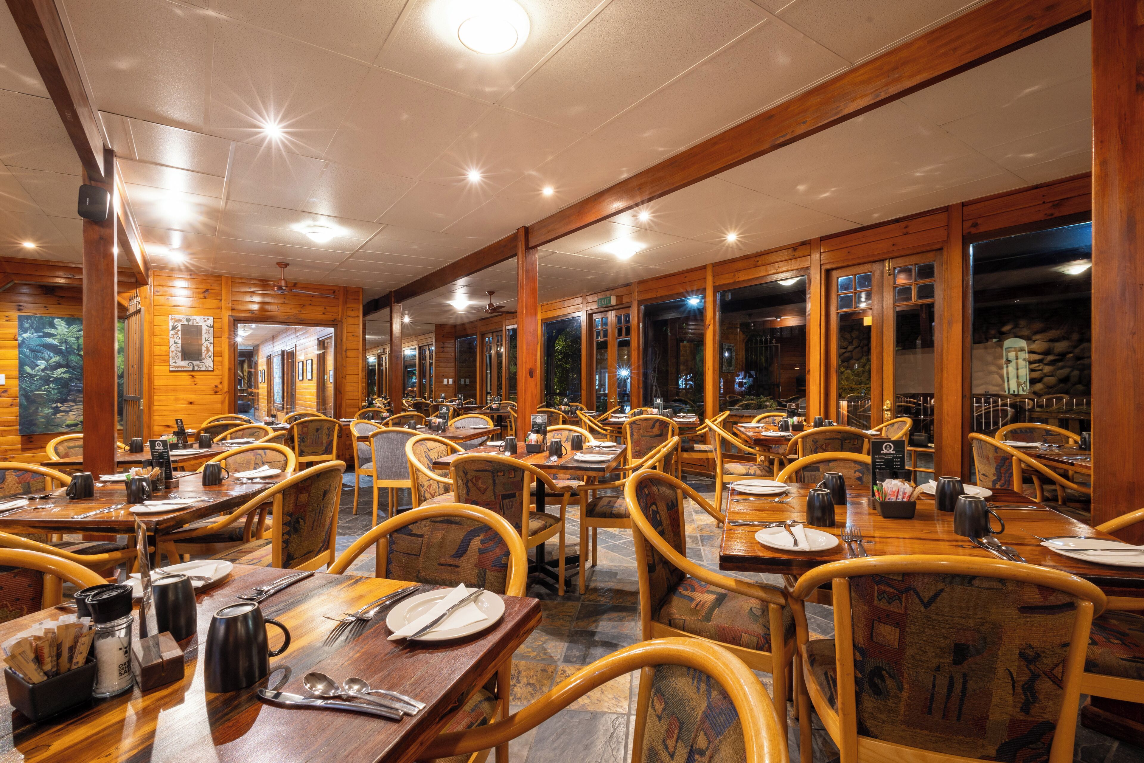 A restaurant with wooden interior, multiple tables and chairs, and a view through the windows.
