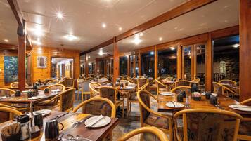 A restaurant with wooden interior, multiple tables and chairs, and a view through the windows.