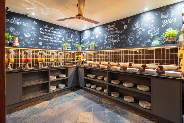 Una barra de desayuno con diversos alimentos y una pared de pizarra con dibujos y texto relacionados con la comida.