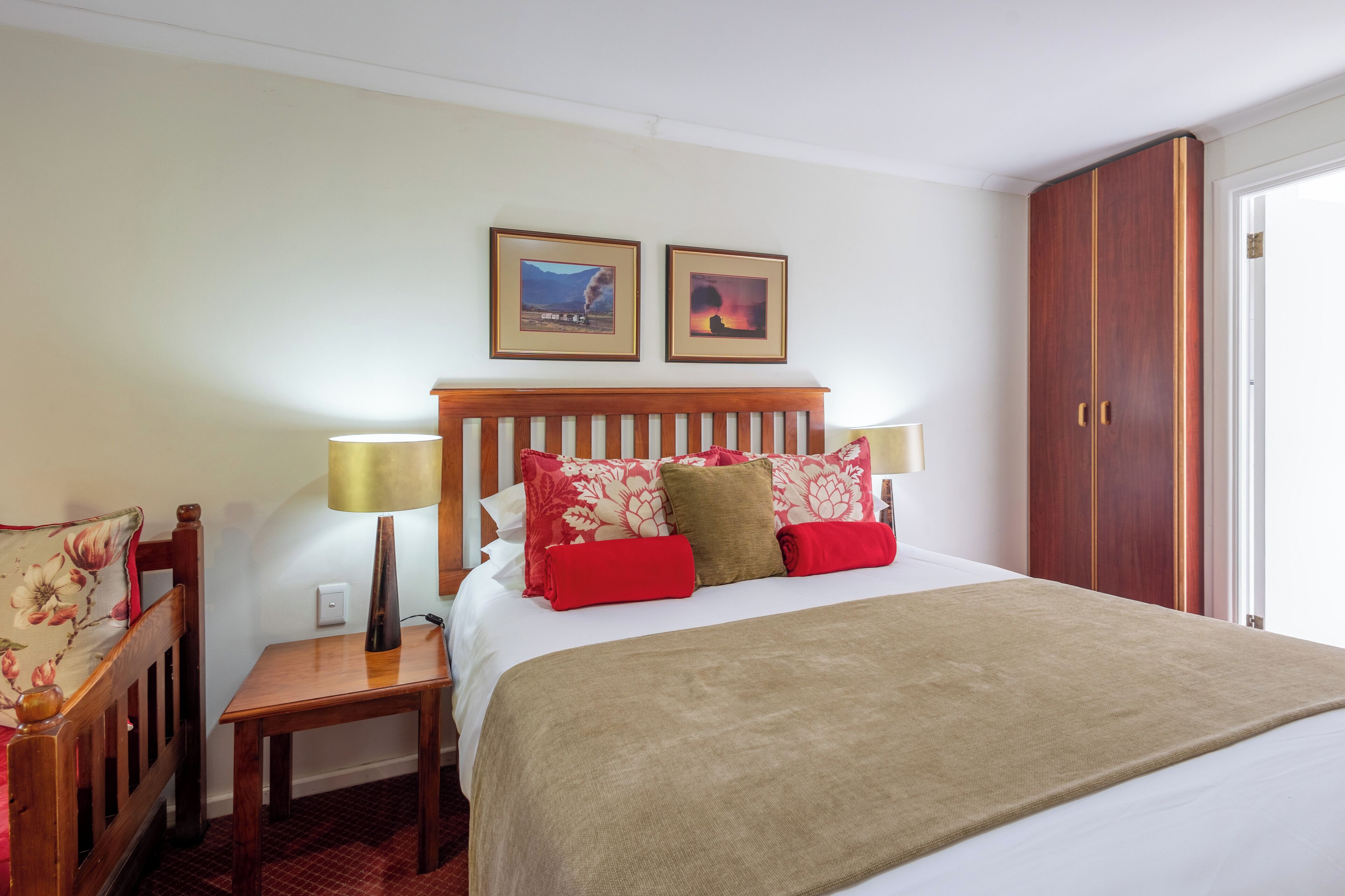 A hotel room with a bed, two bedside lamps, a wooden nightstand, a chair, a wardrobe, and two framed pictures on the wall.
