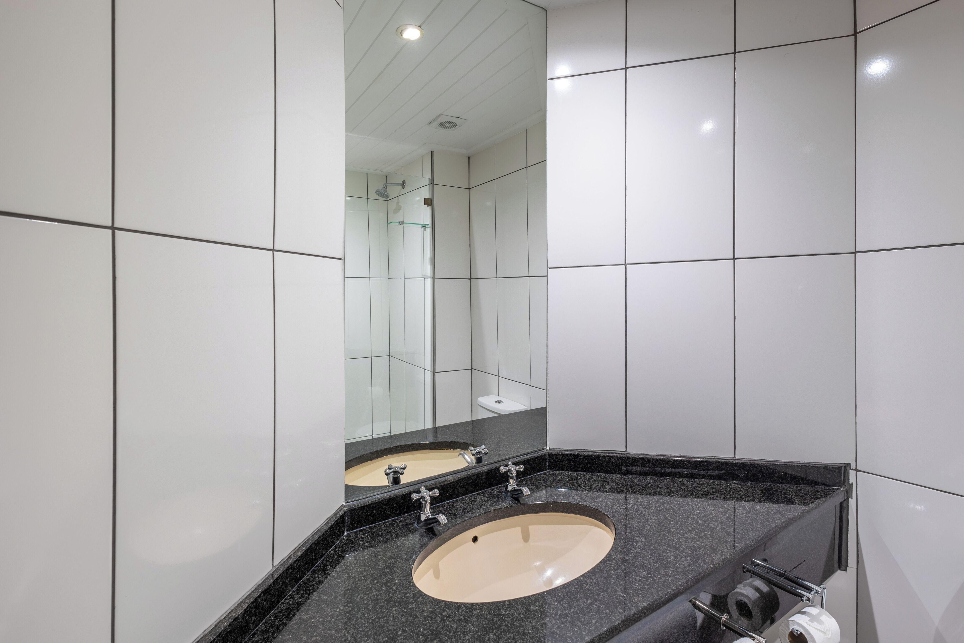 Un baño moderno con un espejo grande, un lavabo color beige y una encimera negra.