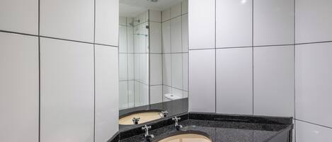 Un baño moderno con un espejo grande, un lavabo color beige y una encimera negra.