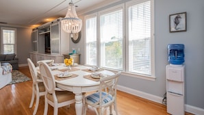 A dining area with a white table, chairs, and a chandelier. There is a water dispenser on the wall. - The Sassy Seahorse: Spacious Beach Home with Multiple Living Areas and Room for (Oak Island)